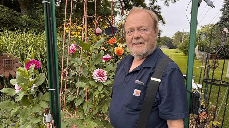 Harry Piehl stands smiling as his dahlias bloom in his garden. 