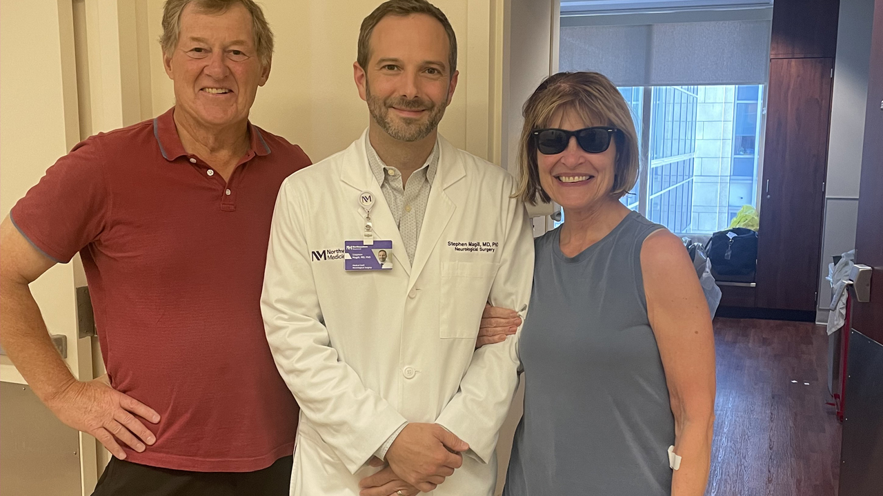 Mark Fenton, Steven T. Magill, MD, PhD, and patient Leslie Fenton stand together smiling at Northwestern Memorial Hospital. 