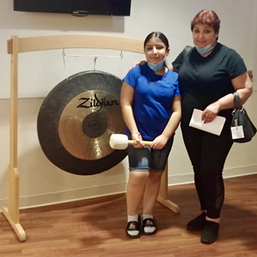 Liliana Castaneda standing near a gong holding a mallet.