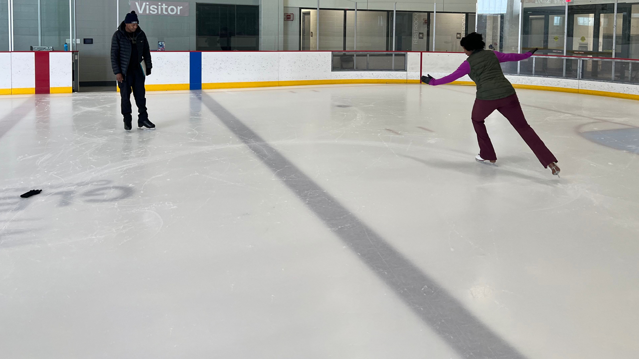 Two people ice-skate at an indoor rink.