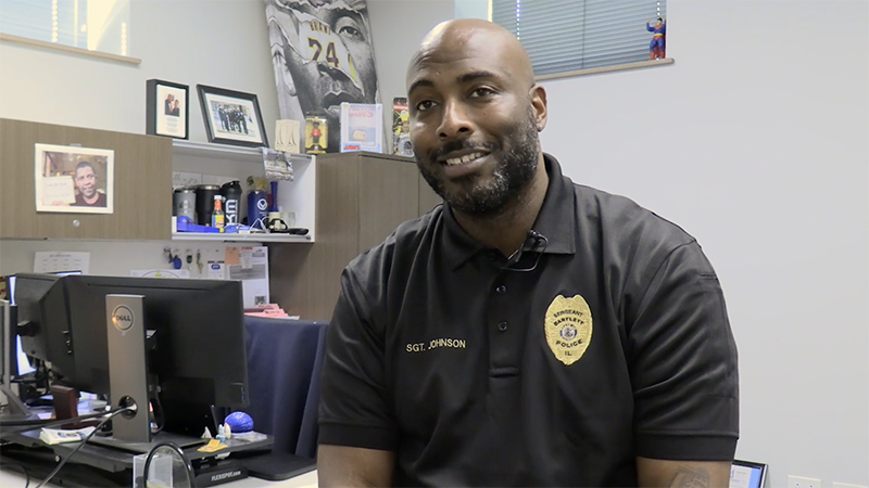 Sergeant Chris Johnson sitting on his desk, smiling. 