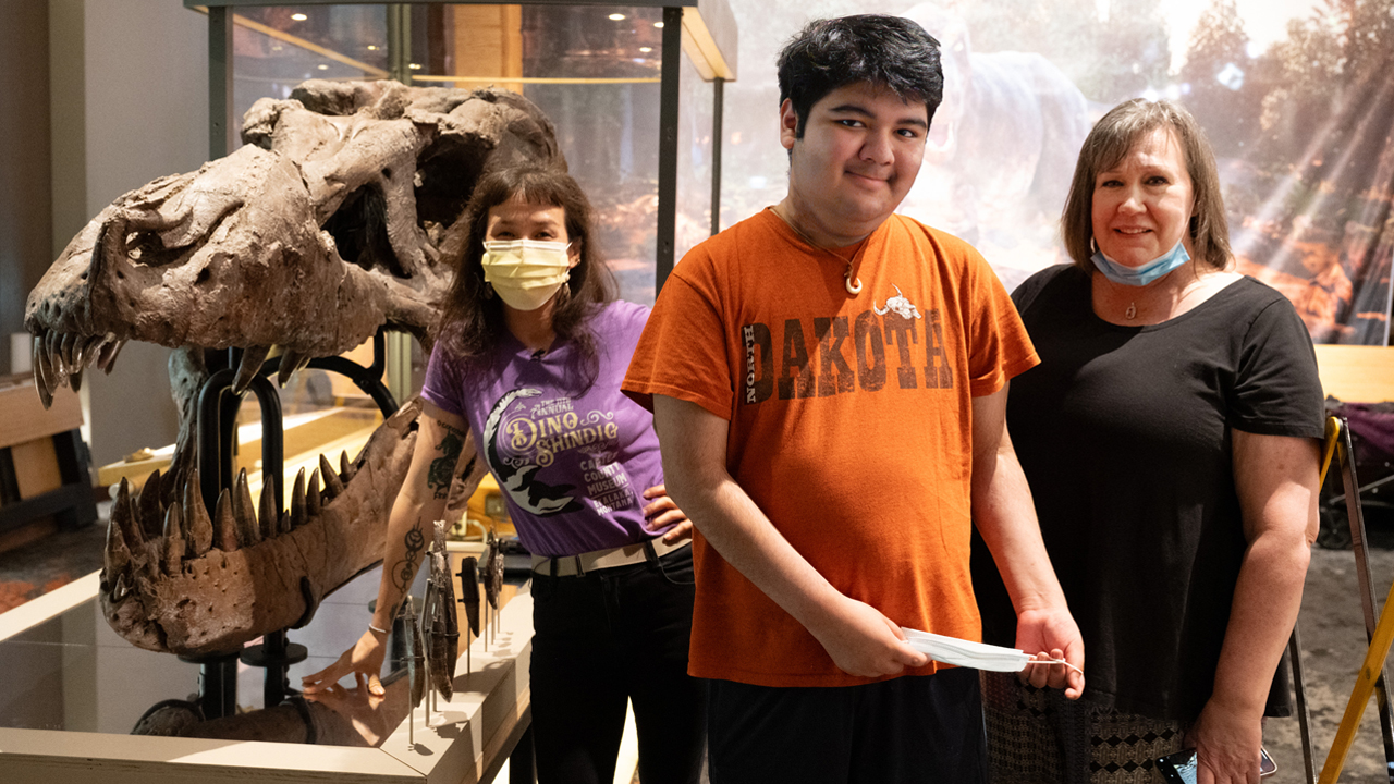 Jingmai Conner, PhD, of the Field Museum, Josh Burton and his mother Kelly Burton, standing next to a Tyrannosaurus rex skull.