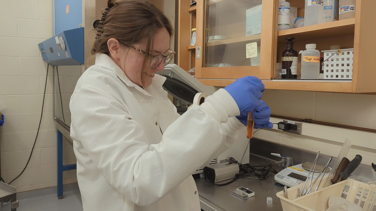 A woman with brown hair wears a white lab coat in a laboratory.