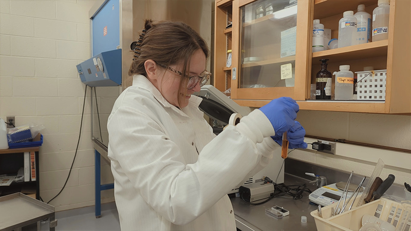 A woman with brown hair wears a white lab coat in a laboratory.