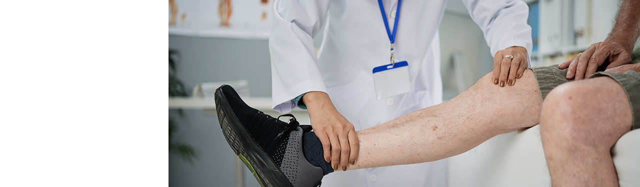 Doctor in lab coat examining patient's leg.