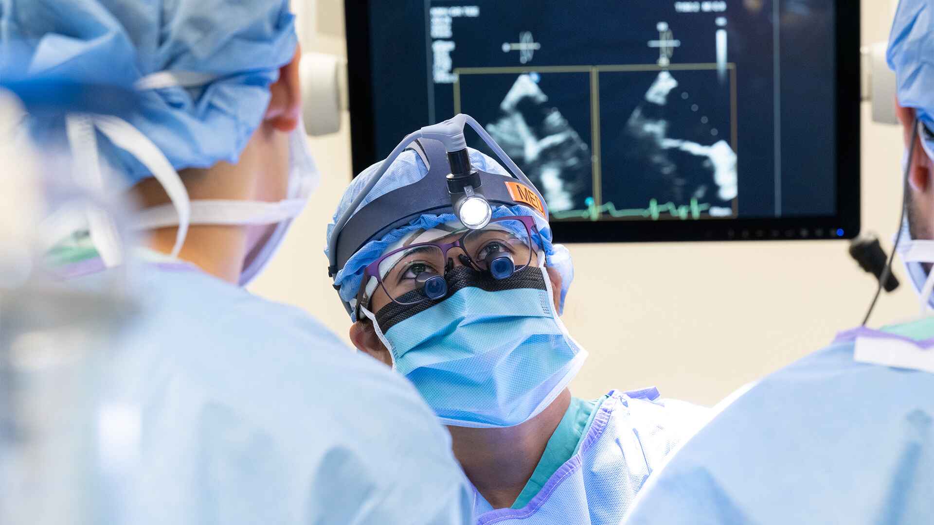 Dr. Melissa Go Medina performing surgery with colleagues in front of an echocardiogram monitor