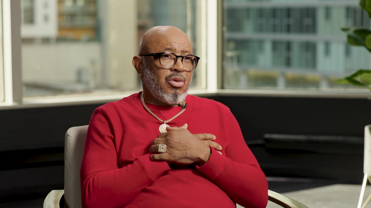 Man in a red sweater talking and folding his hands over his chest