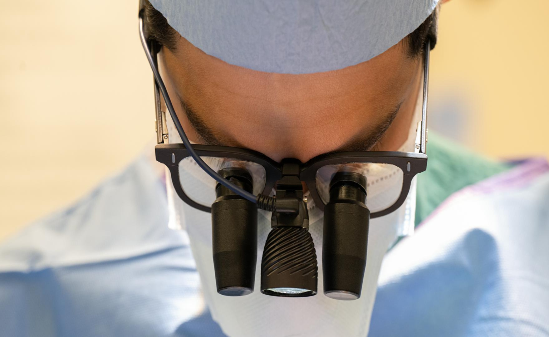 Doctor in mask and scrubs using magnifiers.