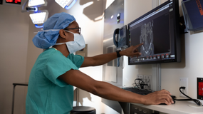 A Northwestern Medicine physician in green scrubs pointing to a lung scan on a computer screen.