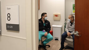 A Northwestern Medicine male physician sitting in an exam room talking to an adult male patient sitting on the exam table.