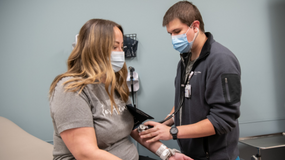 A young woman sitting on an exam table having her blood pressure checked by a male nurse.