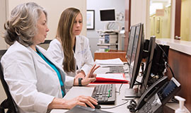 Two physician with the Head and Neck Clinic reviewing medical records at their computers.