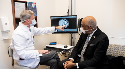 A white male doctor reviewing a medical scan image on a computer with an older African American male patient.