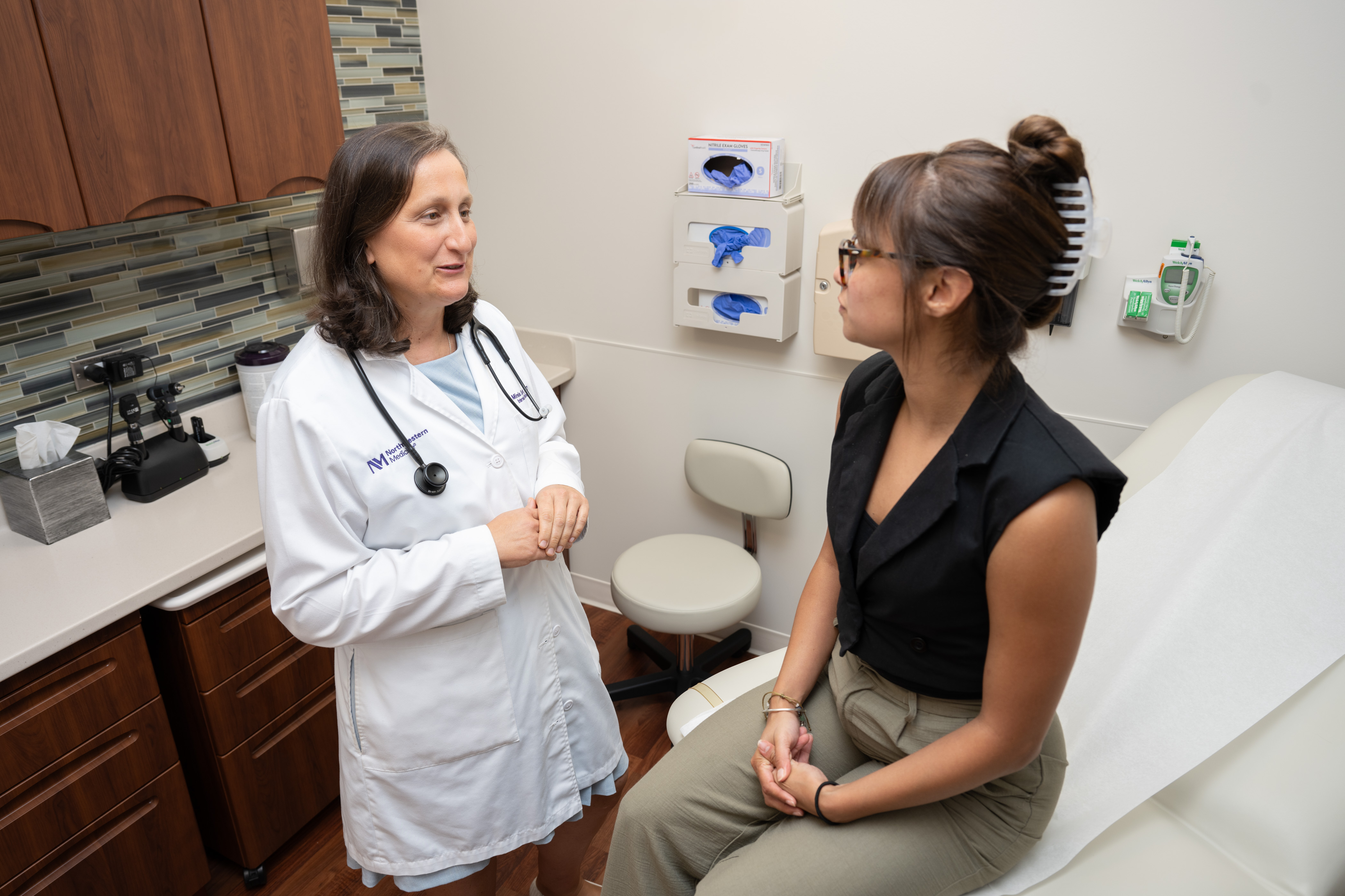 A female Concierge Medicine physician talking with a young woman who is sitting on an exam table.