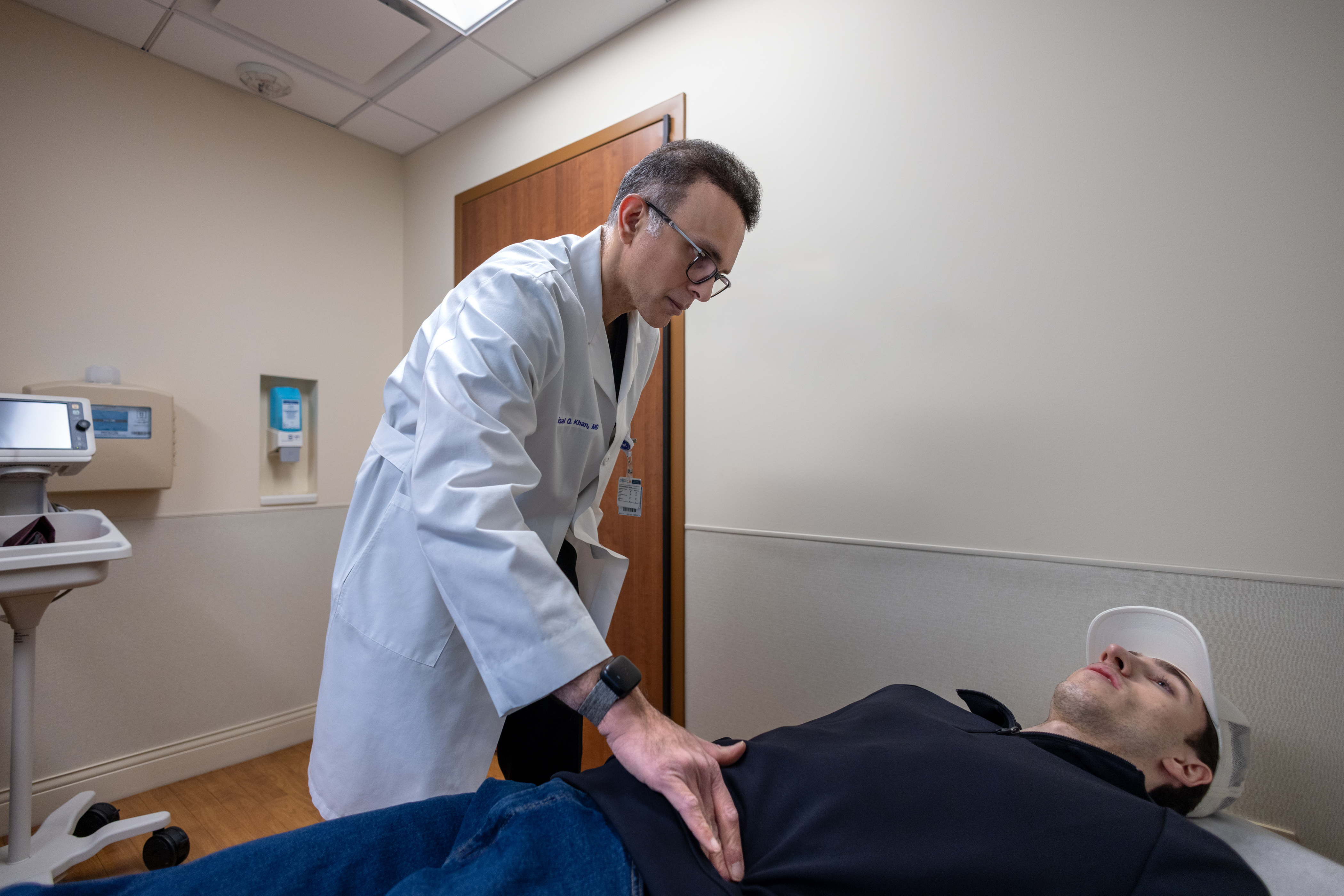 Faisal Qayyum Khan, MD, palpating a patient's abdomen in a medical exam room