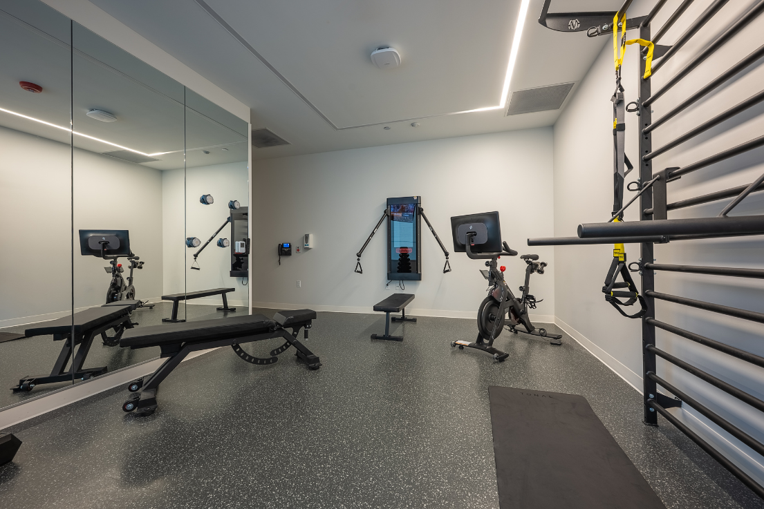 A workout room with exercise machines and mirrors.