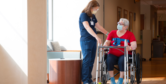 Patient in a wheelchair holding a walker and being assisted by a Marianjoy employee