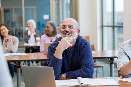 Man in a classroom sitting at a laptop.
