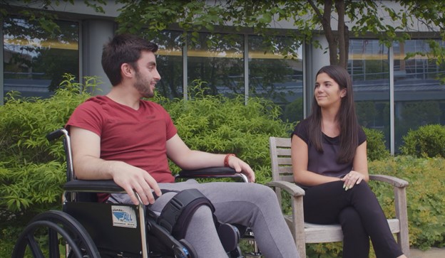 Patient in a wheelchair talking to a visitor in a chair.