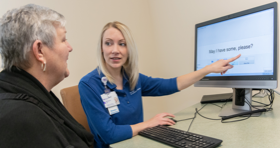 Female clinician pointing at a computer and helping a female patient in a black shirt