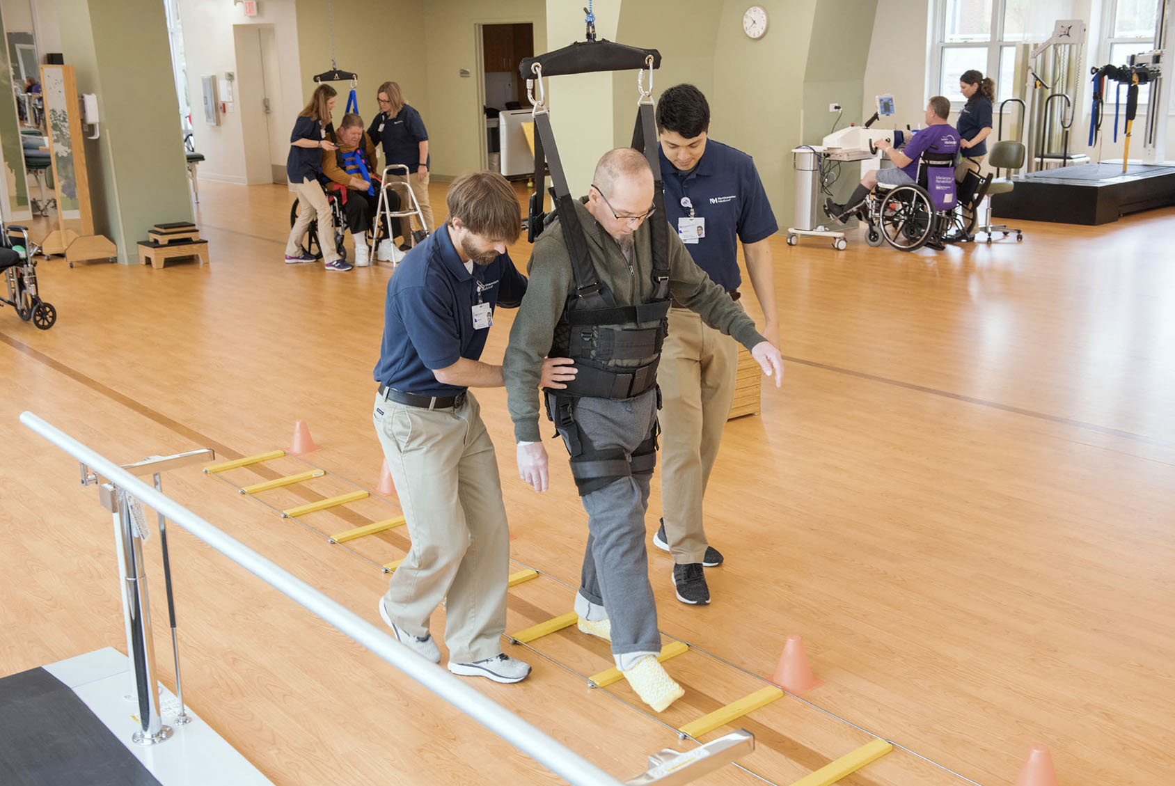 Clinicians helping patient to walk using an assistive device suspended from the ceiling.