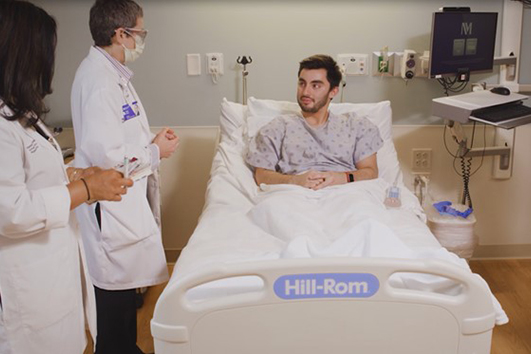 Patient in bed. Two Marianjoy employees are standing at his side.