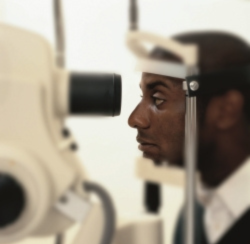An African American male patient with his face in a machine used for an eye exam.
