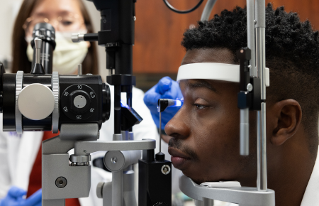 Patient receiving an eye examination with a slit lamp while a clinician performs the exam.