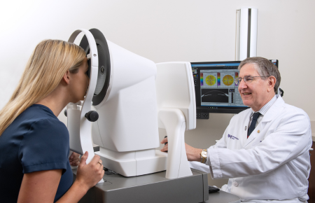 A laser vision correction physician is performing an eye exam on a young woman.