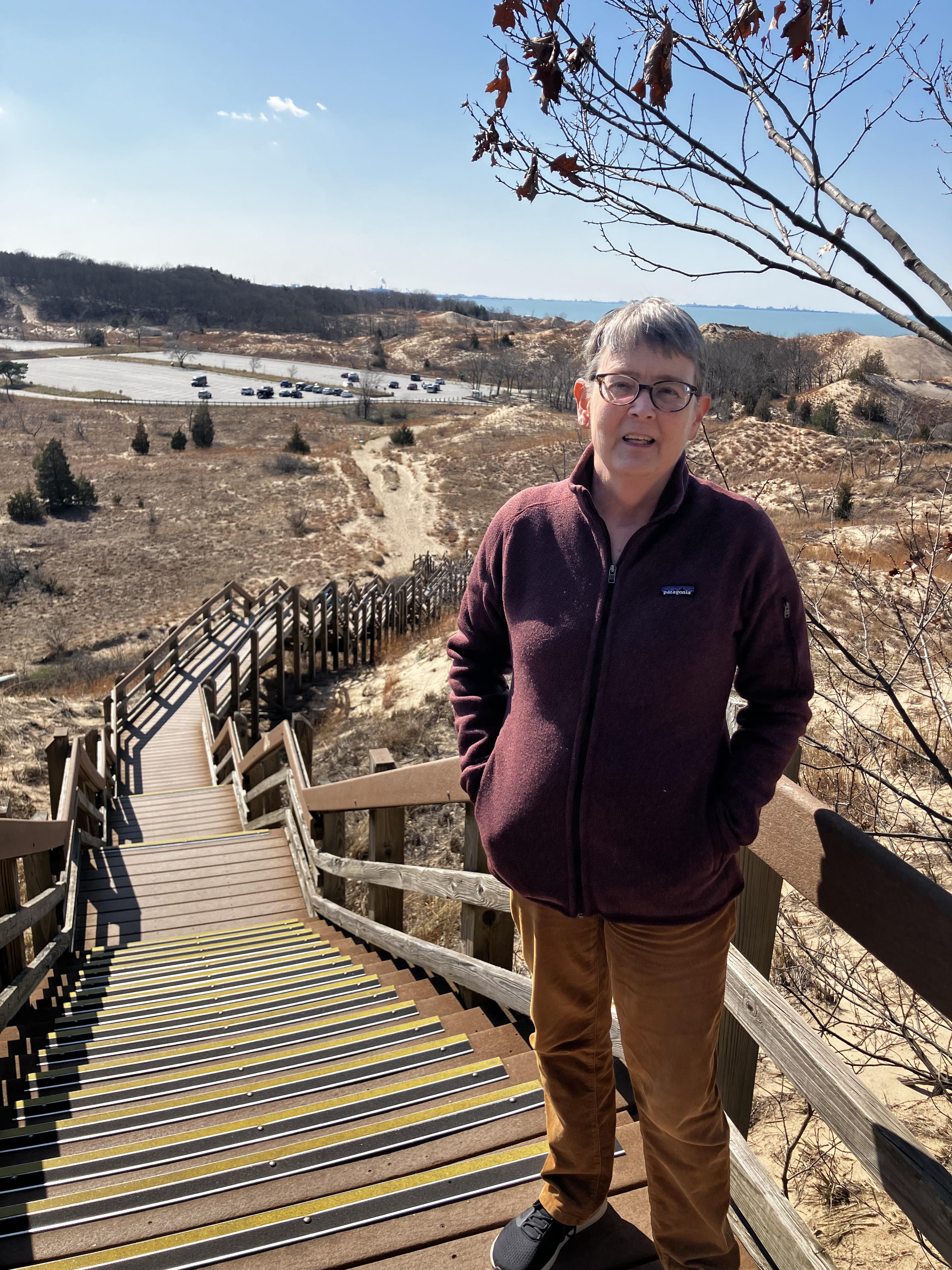 Lung transplant recipient standing on a stairway overlooking sand dunes and a lakeshore during an outdoor hike.