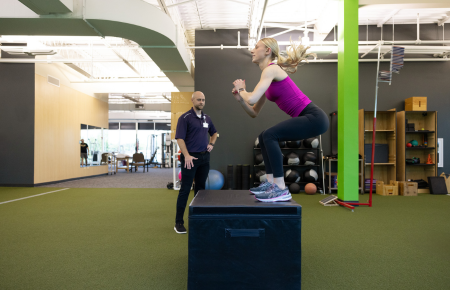 A young woman doing box jumps with an athletic trainer.