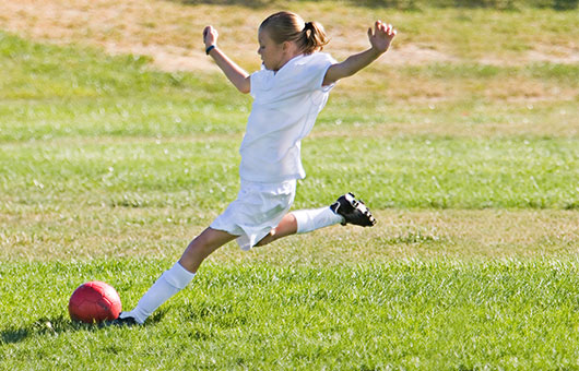 Girl on soccer field kicking ball