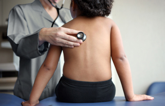Physician using stethoscope to check young boy.