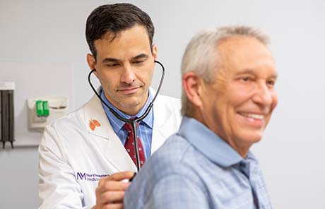 A Northwestern Medicine pulmonary physician listening to a male patient's chest.