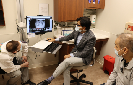 Dr. Ankit Bharat looking at a computer screen of a lung X-ray with two other men in a patient exam room.