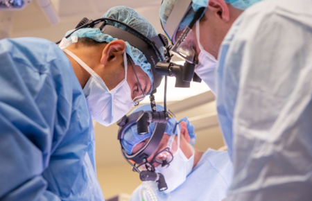 Three male physicians in surgical scrubs, masks and eye protection performing a surgery.