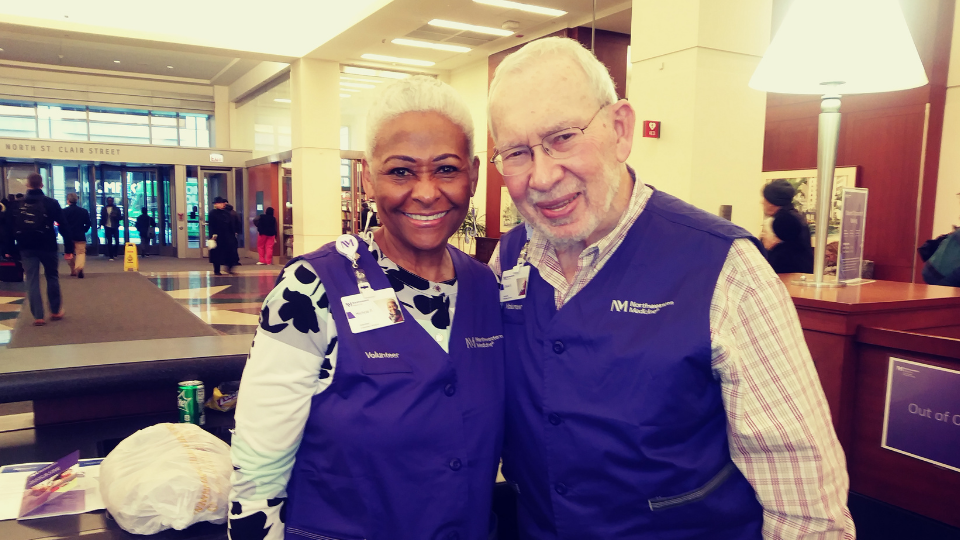 A man and woman smiling during their Northwestern Medicine volunteer shift at the information desk.
