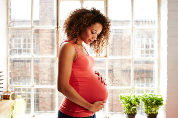 Pregnant woman standing near a window, looking down at her belly bump