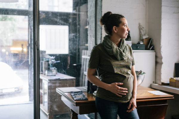 Pregnant woman in her downtown apartment, looking out a window