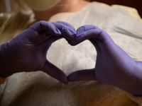 A person wearing purple medical gloves making the shape of a heart with their hands.