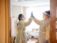 Two female nurses wearing yellow scrub coverings sharing a high-five.