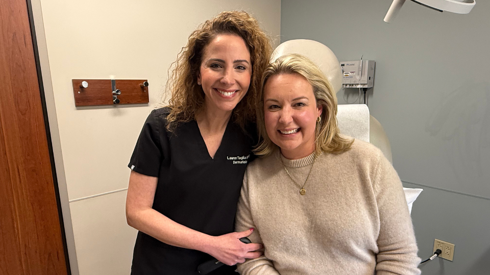 Dermatology clinician and patient pose together in an exam room.
