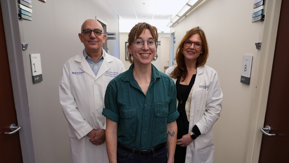 Patient stands with two members of a care team in a clinic hallway.
