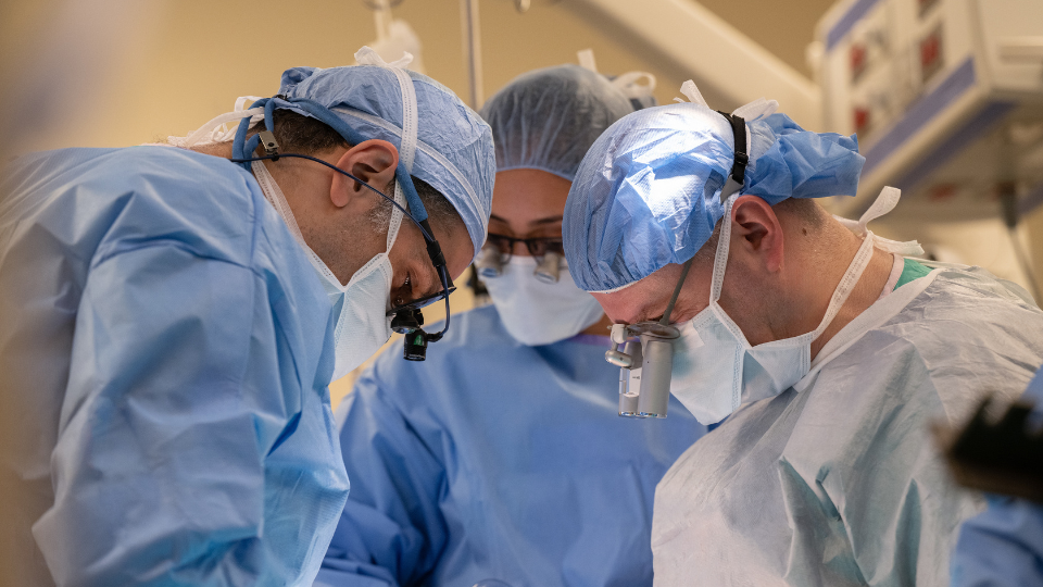 Surgeons wearing protective equipment perform a procedure in an operating room.