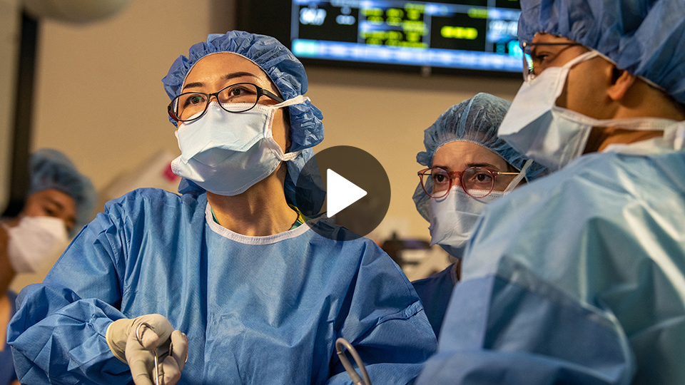 A female surgeon wearing blue scrubs and a surgical mask performing an operation.