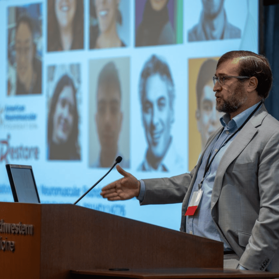 Man standing behing a podium giving a talk at the AI conference. In the background is a presentation.