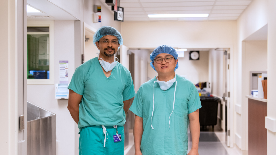 Two surgeons in scrubs standing in a hallway.