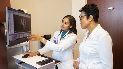 Two female Northwestern Medicine physicians wearing white lab coats looking at an ultrasound image on a computer screen.