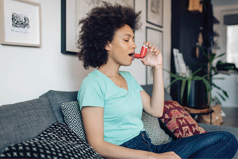 Young African-American woman using asthma inhaler at home.