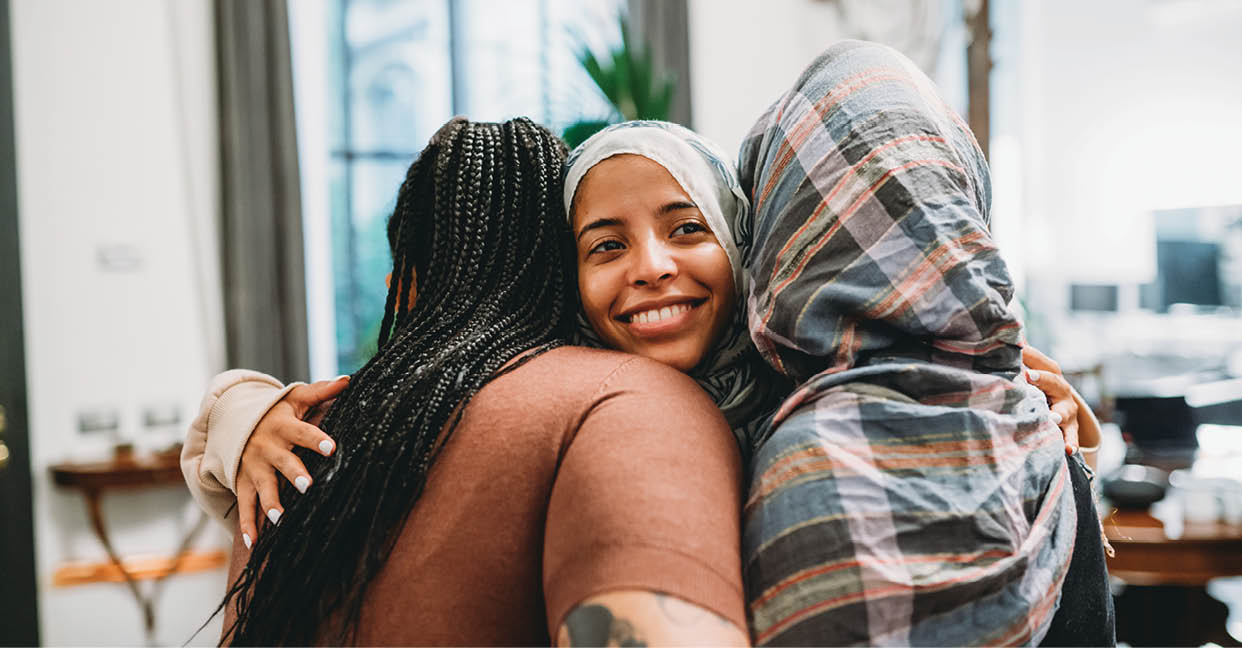 Close up shot of three friends embracing each other. They are smiling, supporting each other.